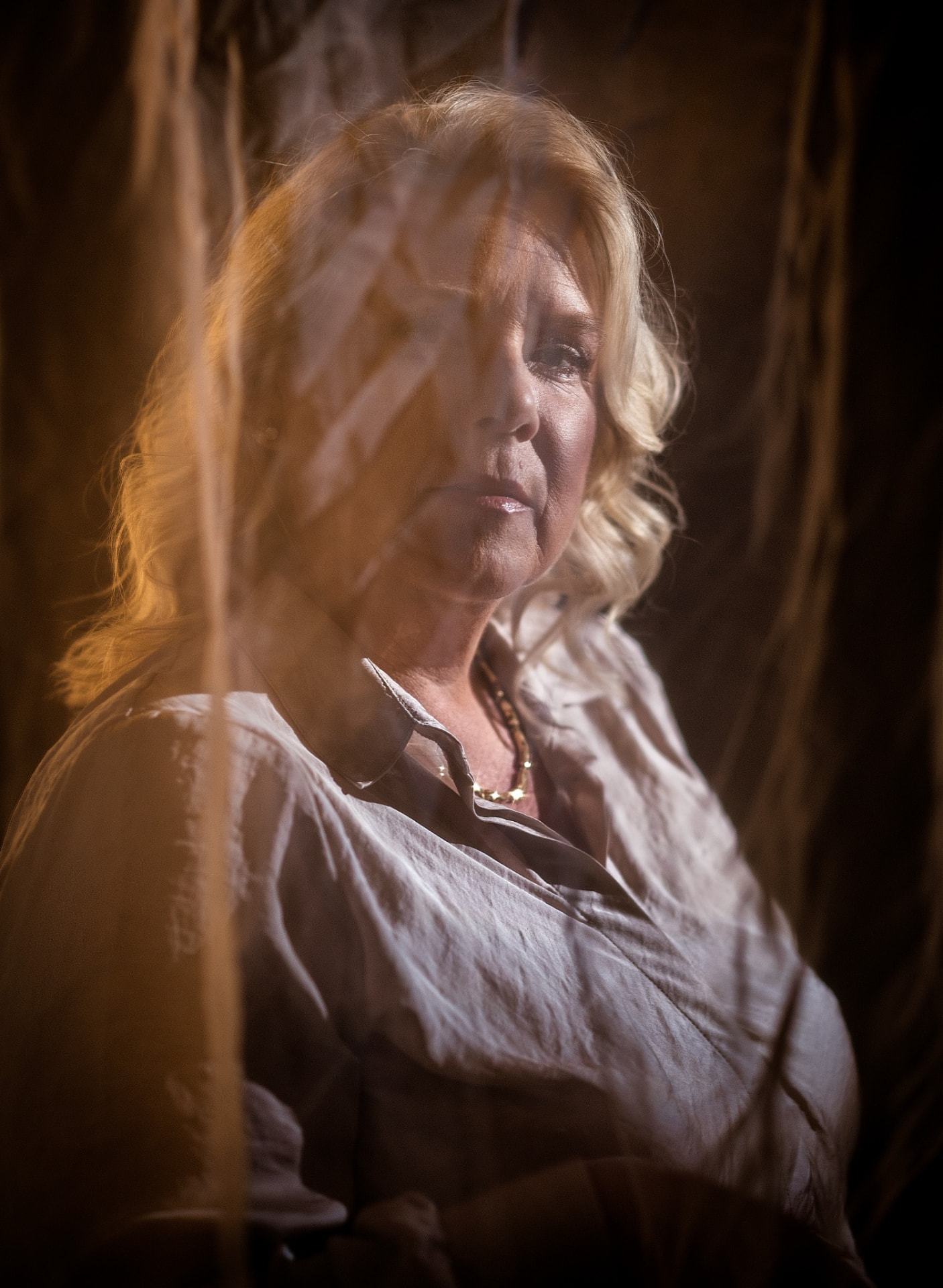 Camilla in low light seen through hanging fabric